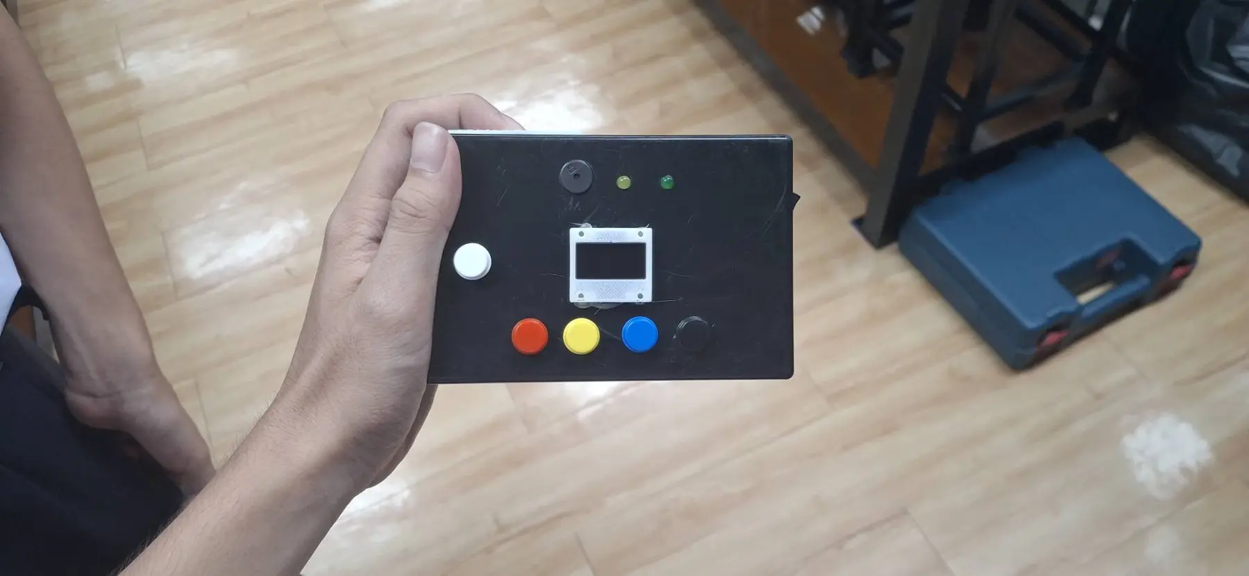 A student holding the first Emotion Sync prototype, showing its OLED screen and four colored response buttons
